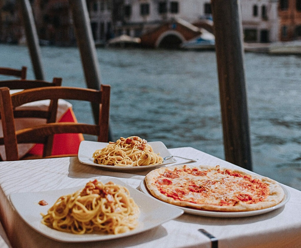 Delightful Italian pasta and pizza served by the scenic Venetian canal under sunny skies.